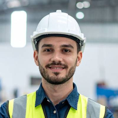 Ein Mann, der einen weißen Schutzhelm, eine gelbe Sicherheitsweste und ein blaues Hemd trägt, lächelt in einer Industrieumgebung in die Kamera und verweist auf moderne Arbeitsplätze, an denen Online-Notardienste wichtige Dokumente vereinfachen können.