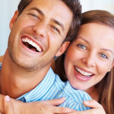 Ein lächelnder Mann und eine lächelnde Frau umarmen sich eng, beide schauen in die Kamera und strahlen Glück aus - wie neue Partner, die ihr erstes gemeinsames Geschäftskonto GmbH UG feiern. Der Mann trägt ein blau gestreiftes Hemd und die Frau steht etwas hinter ihm.