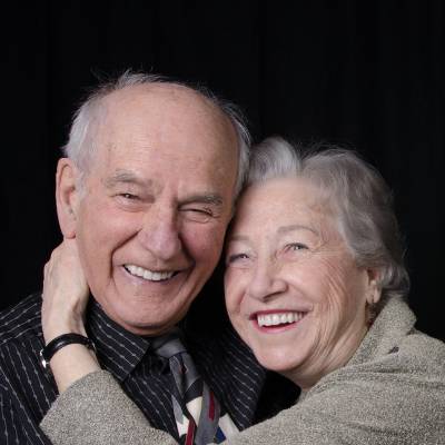 Ein älteres Paar lächelt herzlich und umarmt sich. Der Mann mit gestreiftem Hemd und Krawatte und die Frau im hellen Pullover freuen sich wie Partner, die gemeinsam einen reibungslosen Gesellschafterwechsel oder GmbH-Anteilsverkauf feiern.