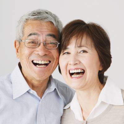 Ein älteres Paar mit kurzen Haaren, das helle Oberteile trägt, lächelt und lacht zusammen, während es der Kamera zugewandt ist und seine eintragungsmitteilung handelsregister gmbh ug vor einem schlichten Hintergrund feiert.