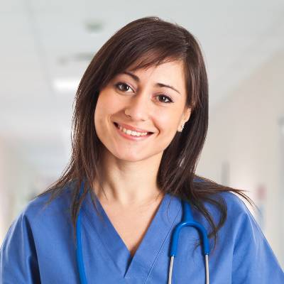 Eine junge Frau in blauem Arztkittel und mit Stethoskop steht mit einem warmen Lächeln in einem hellen Krankenhausflur - ein stolzes Teammitglied, das seine Rolle bei der Kettengründung mit Mitgefühl und Fachwissen ausfüllt.