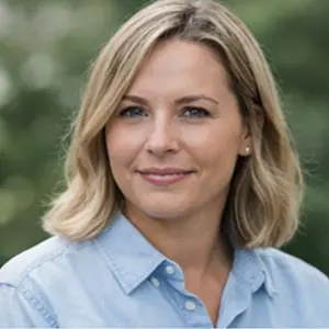 Eine Frau mit blondem, schulterlangem Haar und einem hellblauen Button-up-Hemd lächelt sanft in die Kamera. Der Hintergrund im Freien ist unscharf begrünt und vermittelt eine ruhige Atmosphäre - perfekt für eine Diskussion darüber, wie die GmbH gründen Berlin.