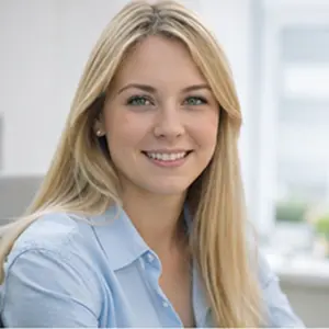 Eine junge Frau mit langen blonden Haaren und einem hellblauen Hemd sitzt lächelnd in einem hellen, modernen Büro und berät in Sachen Geschäftsführerwechsel Notar Berlin.