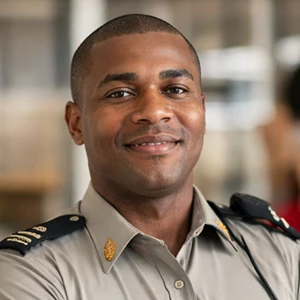 Ein Mann mit mittellangen lockigen dunklen Haaren und einem Bart lächelt in die Kamera. Er trägt ein dunkelblaues Hemd und steht vor einem unscharfen hellen Hintergrund, als sei er bereit für einen Termin bei einem Notar der Immobilien Schenkung in Berlin.