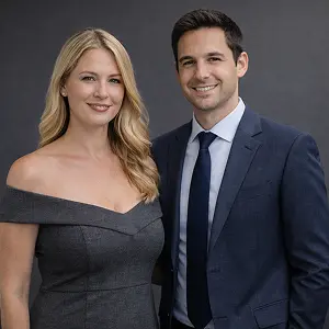 Eine Frau in einem schulterfreien grauen Kleid und ein Mann in einem dunklen Anzug mit Krawatte stehen nebeneinander und lächeln zuversichtlich, als ob sie bereit wären, in Berlin eine GmbH zu gründen, vor einem schlichten dunklen Hintergrund.