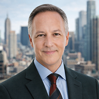 A middle-aged man in a suit and tie smiles at the camera. He is standing in front of a city skyline that may represent a notary in Berlin, with tall buildings and a partly cloudy sky in the background.