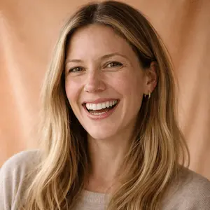 Eine Frau mit langen blonden Haaren und einem hellen Pullover lächelt breit vor einem pfirsichfarbenen Hintergrund. Das spiegelt die Zuversicht wider, die man nach einer dauerhaften handelsregistereintragung in Berlin verspürt.