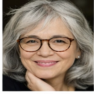 Eine lächelnde ältere Frau mit grauen Haaren und Brille stützt ihr Kinn auf ihre Hand, vielleicht beim Brainstorming von Ideen für Online-Gründungen. Sie trägt ein schwarzes Oberteil und kleine Ohrringe.