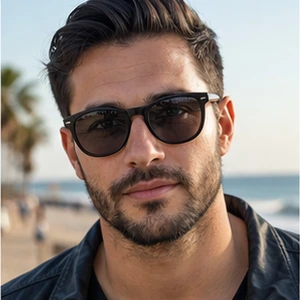 Ein Mann mit kurzen dunklen Haaren, gestutztem Bart und Sonnenbrille - gekleidet in eine schwarze Jacke - steht an einem Strand mit Palmen und dem Meer im Hintergrund und strahlt die Zuversicht eines Rechtsanwalts Strafrecht aus, der eine Auszeit genießt.